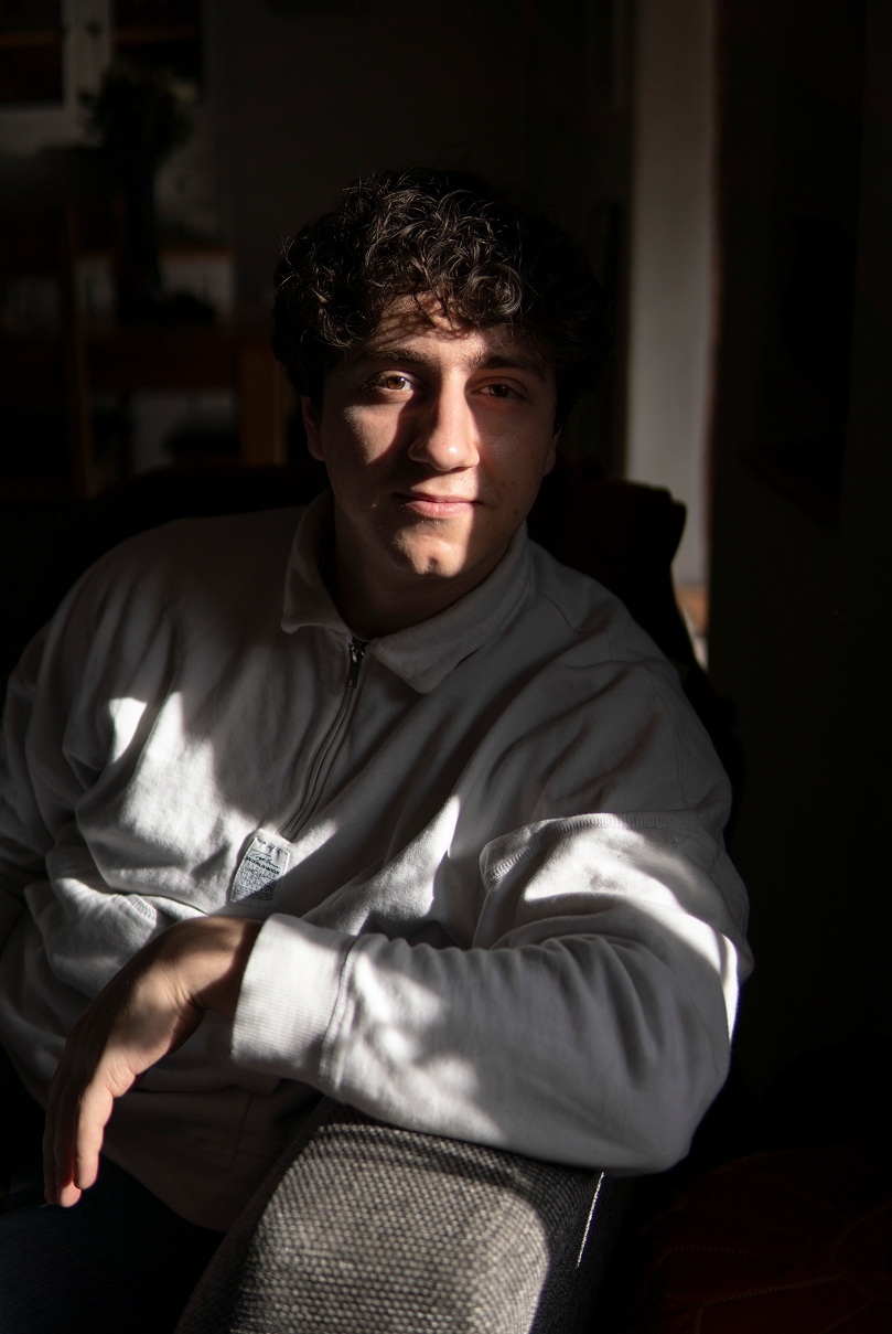 A man staring at the camera with patches of light being cast onto his body and face.