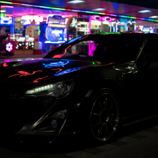 A car outside an arcade, being illuminated by it's lights.